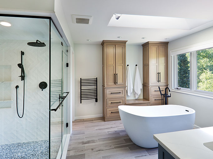 Modern bright bathroom with freestanding white tub, glass walk-in shower, wooden storage cabinets and skylight