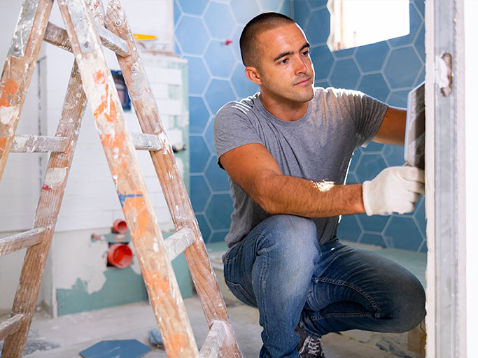 A man installing blue hexagon wall tiles in a bathroom during home renovation.