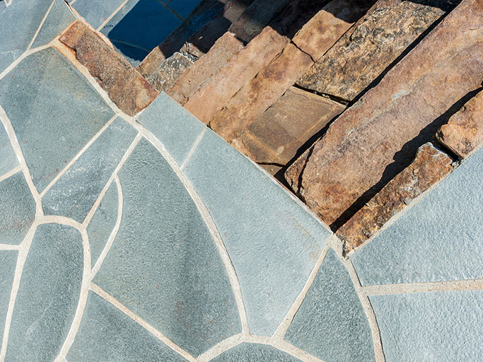 Outdoor blue-gray irregular flagstone patio meeting stacked brown natural stone steps