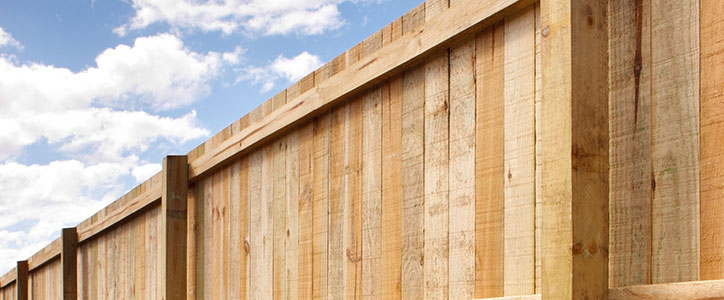 New wooden privacy fence with vertical planks under a blue sky with scattered clouds