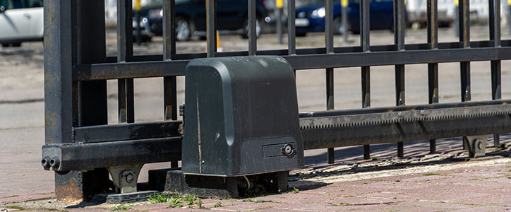 Automatic sliding security gate with electric drive motor at base on paved driveway