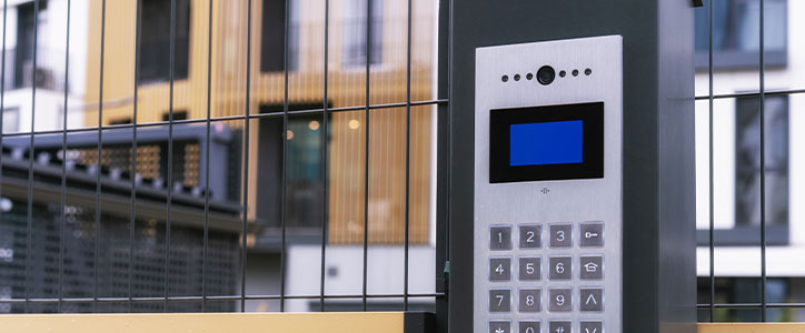 Keypad entry intercom with blue display at gated modern residential building entrance
