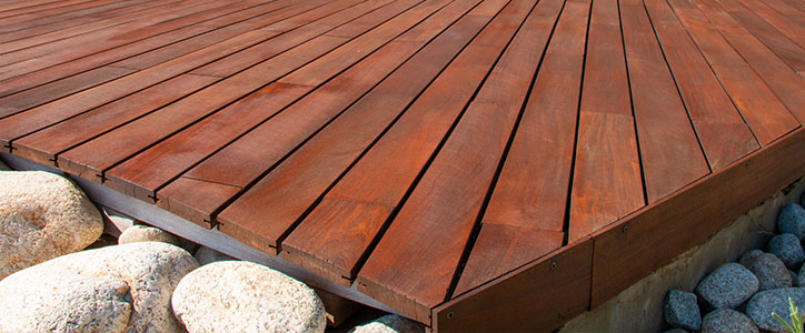 Corner of a red-brown wooden deck with parallel planks over landscaping river rocks