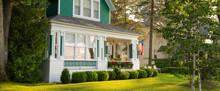 Green-and-white two-story house with enclosed front porch, American flag and manicured lawn.