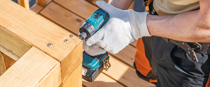 Construction worker wearing gloves using a cordless drill to fasten wood deck railing