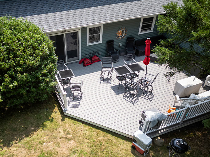 Aerial view of a gray backyard deck with patio tables, chairs, red umbrella, grill and cooler