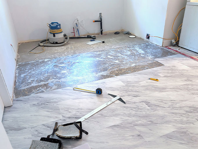 Room mid-renovation with marble-look vinyl plank flooring partially installed and flooring tools scattered on subfloor