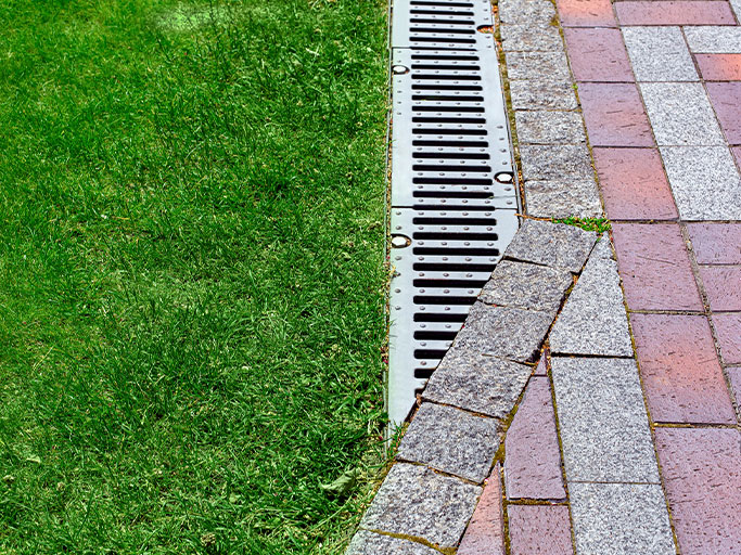 Lush green lawn bordered by metal drainage grate and curved stone-and-brick pathway