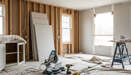 Home renovation interior with exposed studs, drywall sheets, miter saw and power tools on drop cloths