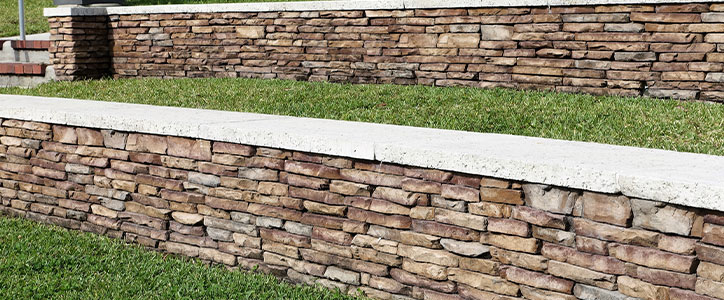 Terraced stone retaining walls with concrete caps and lush lawn in a residential landscape
