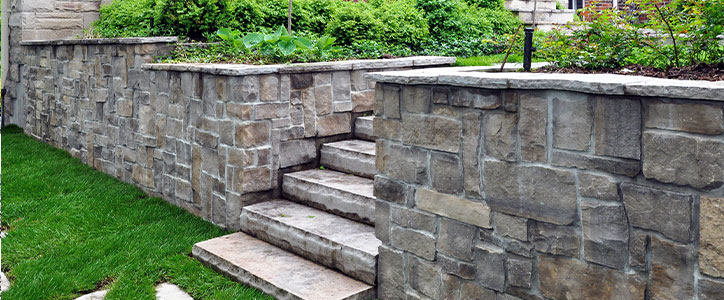Stone retaining wall with wide stone steps, manicured green lawn and shrubs in residential landscape