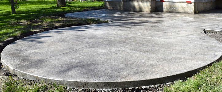 Fresh circular concrete patio slab in a grassy park setting with surrounding trees and landscaping