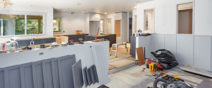 Open-plan kitchen renovation with gray wainscoting, cabinets and scattered tools and materials
