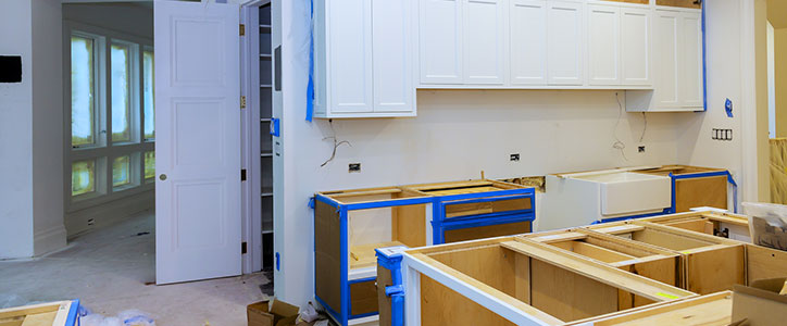 Kitchen remodel in progress: open lower cabinet frames, white upper cabinets installed, blue painter's tape