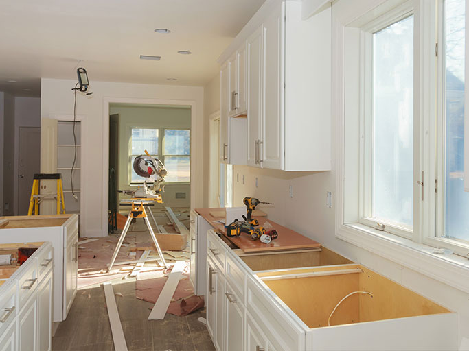 Kitchen under renovation with white cabinets, open sink cabinet, power tools and a miter saw on a stand