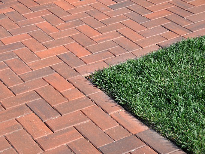 Herringbone red brick walkway bordering a neatly trimmed green grass lawn