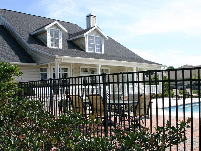 Suburban two-story house with swimming pool and patio dining set visible behind a black metal fence