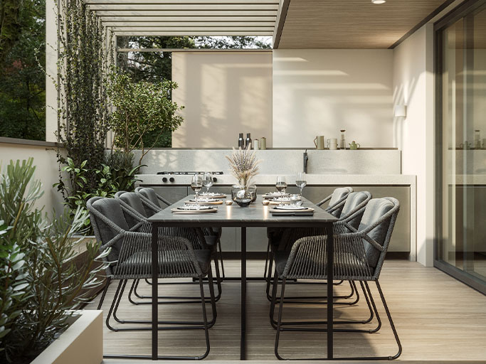 Modern outdoor dining area: black table set for eight on covered patio with cushioned chairs, plants and built-in kitchenette.