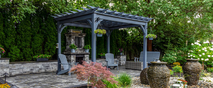 Backyard patio with pergola, stone fireplace, Adirondack chairs, potted plants and water urns in landscaped garden