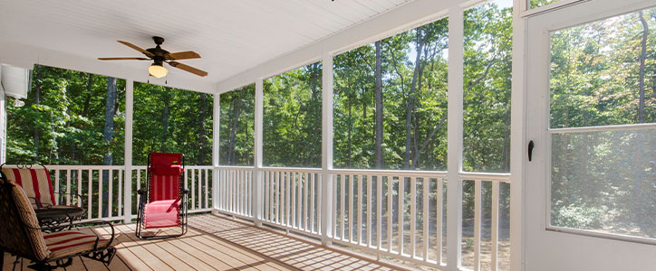 Sunny screened porch with wooden deck, ceiling fan, outdoor seating and views of wooded backyard.