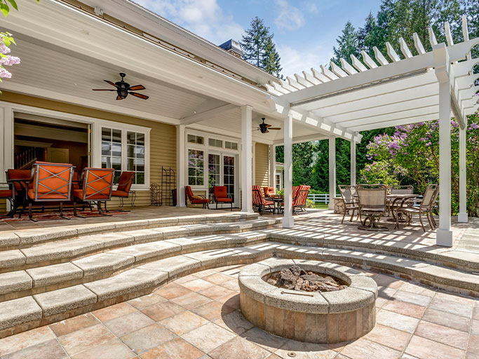 Luxury backyard patio with pergola, stone fire pit, outdoor dining and lounge seating under covered porch