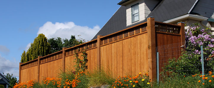 Tall wooden privacy fence along suburban house, bordered by orange and yellow flowers under a blue sky