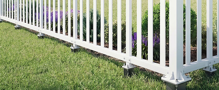 White vinyl picket fence bordering a garden bed with purple flowers and a well-manicured green lawn