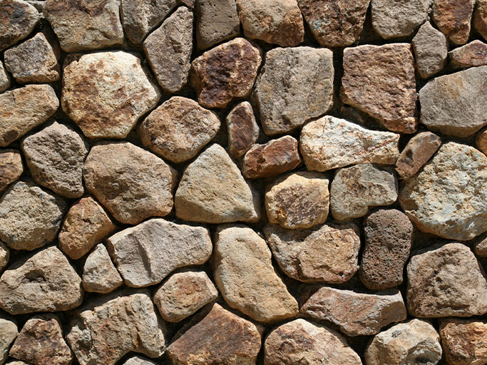 Rustic stacked stone wall of irregular beige and brown rocks forming a textured natural facade