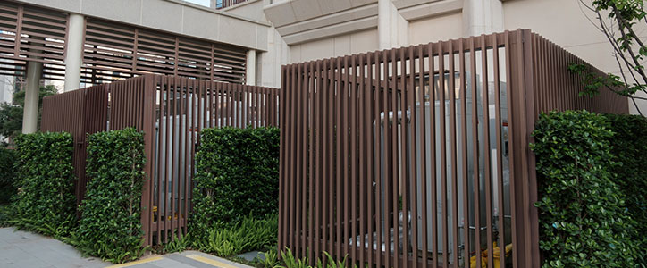 Modern brown vertical slatted privacy enclosures around utility equipment in a landscaped urban courtyard.
