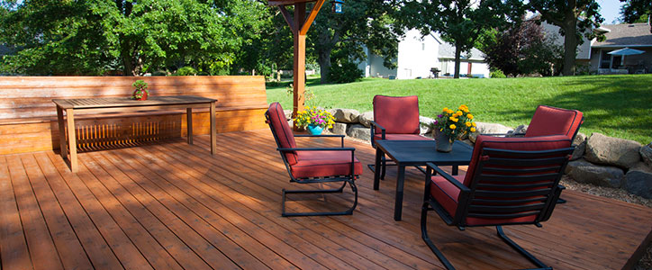 Spacious wooden backyard deck with red-cushioned patio chairs around a table, built-in bench and potted flowers