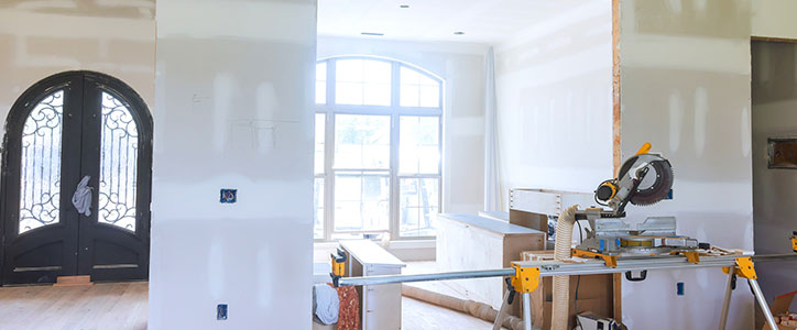Home interior under renovation with drywall, arched window, double front doors and a miter saw on stand.