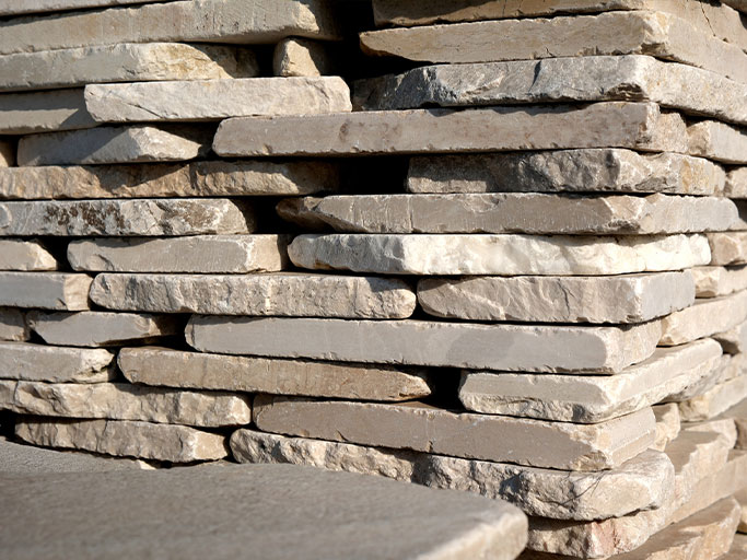 Stacked beige limestone slabs in a neat pile, cut flagstone for landscaping or masonry.