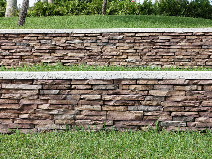 Tiered stacked-stone retaining walls with concrete caps and green grass terraces in a landscaped yard