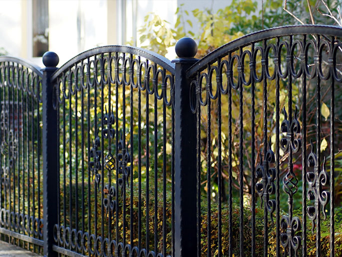 Ornate black wrought-iron garden gate with arched top and decorative scrollwork in leafy yard