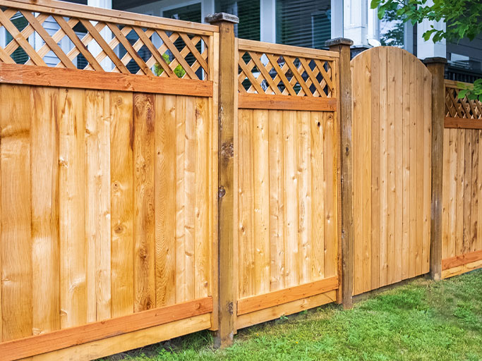 Wooden privacy fence with lattice top and arched gate bordering a residential lawn