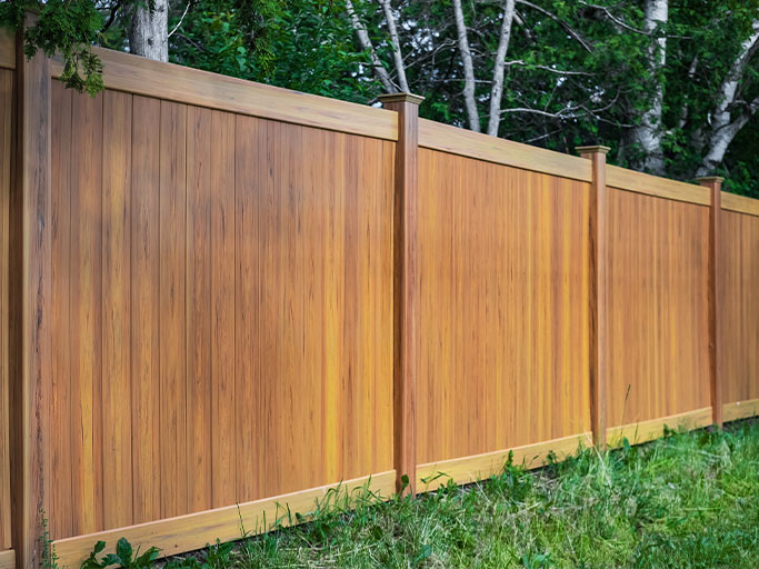 Wooden privacy fence with vertical cedar panels and posts along grassy yard and trees behind